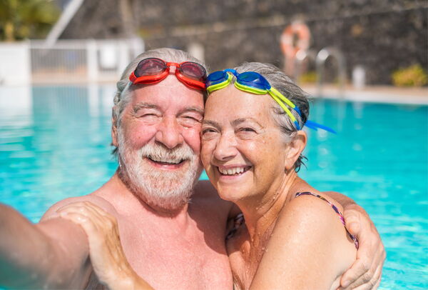 Älteres Paar mit bunten Schwimmbrillen umarmt sich lachend im Außenpool der Solefelsenwelt.